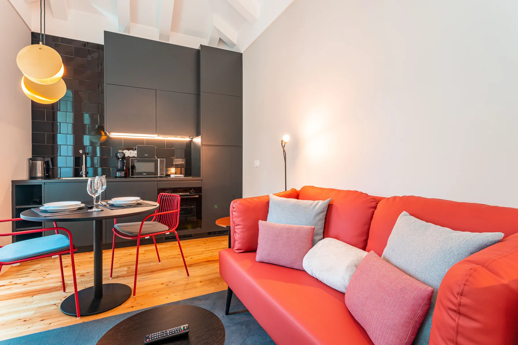Una sala de estar con un sofá colorido junto a una cocina compacta y una mesa de comedor.