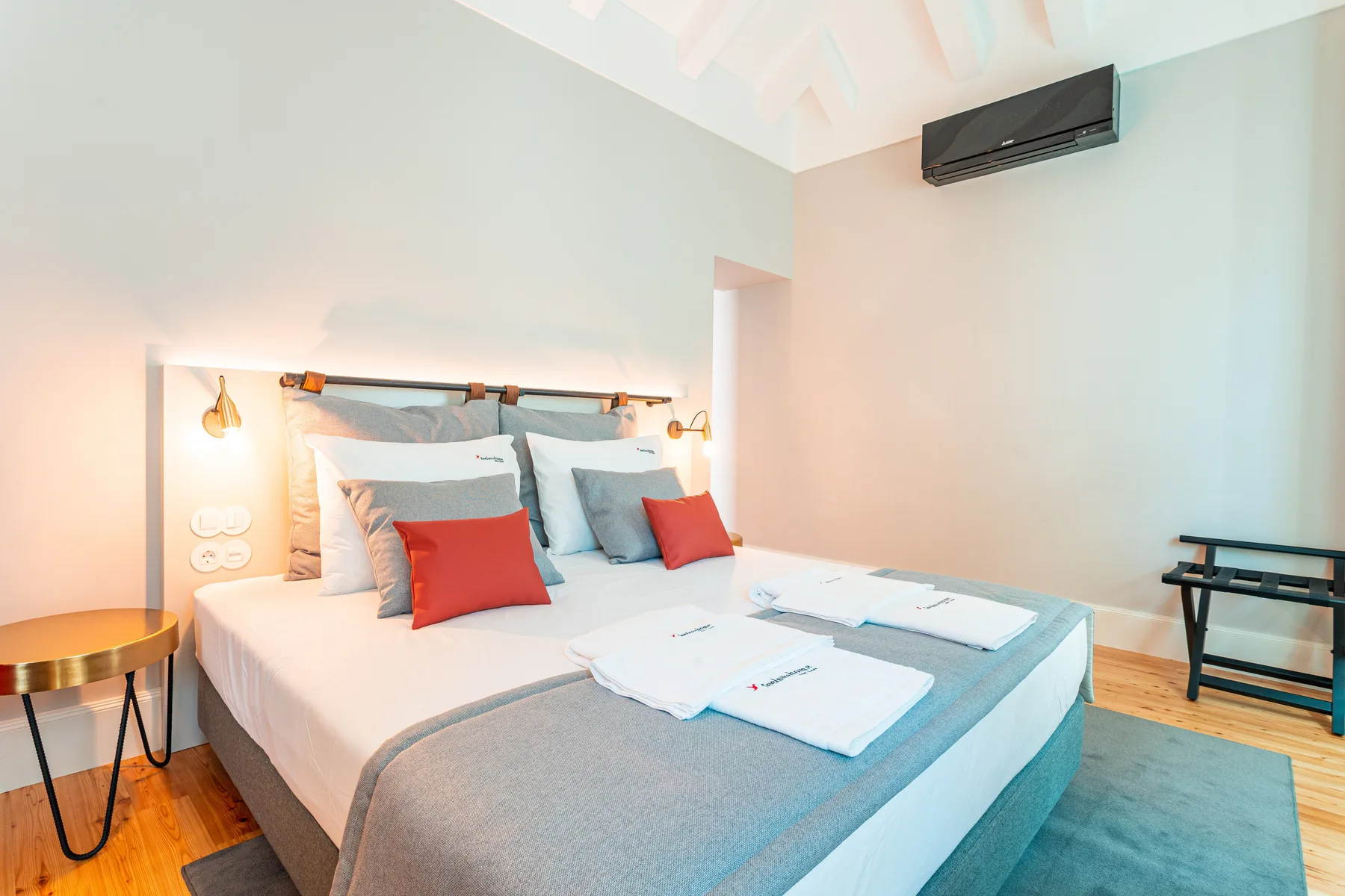 Un dormitorio con una cama bien hecha, toallas dobladas y una mesita auxiliar.