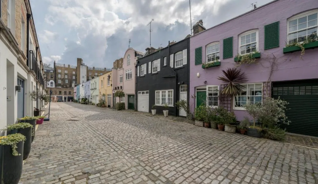 A cobbled street runs between colorful buildings with window boxes and potted plants.