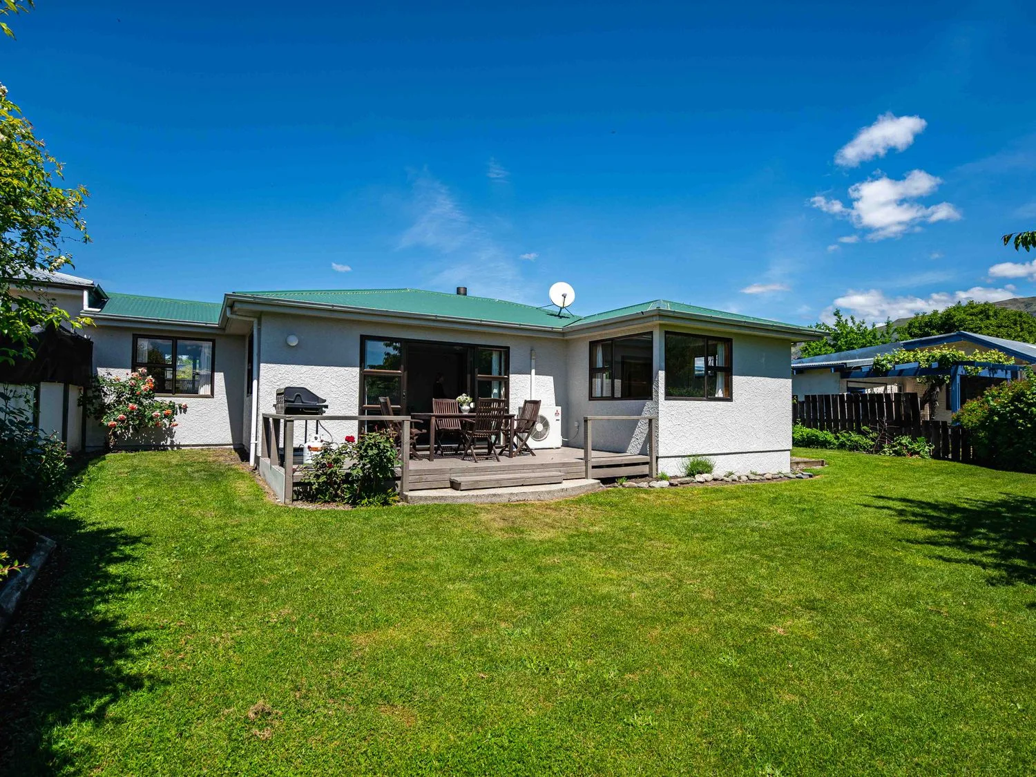 A backyard with a green lawn and a patio with outdoor furniture at Downtown Delight - Wanaka Holiday Home in Queenstown - Wanaka