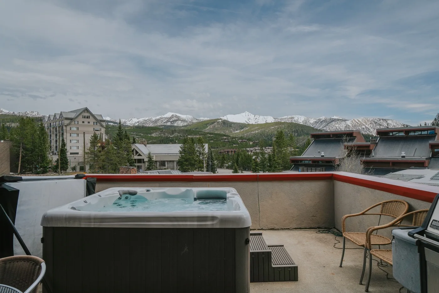 A rooftop terrace features a hot tub and seating with mountains in the distance.