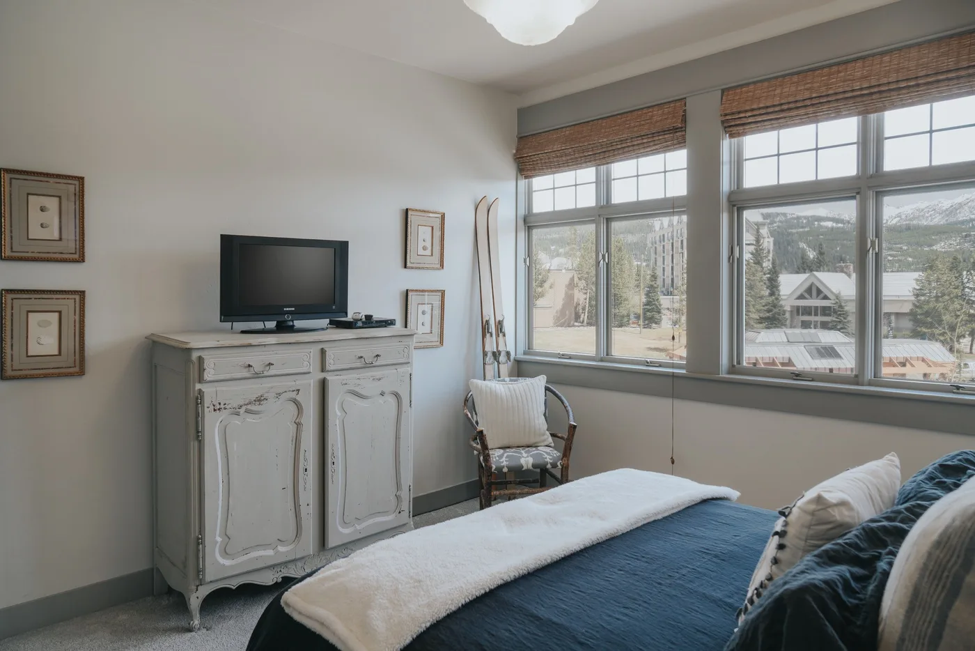 A bedroom with a bed beside a television and large windows.