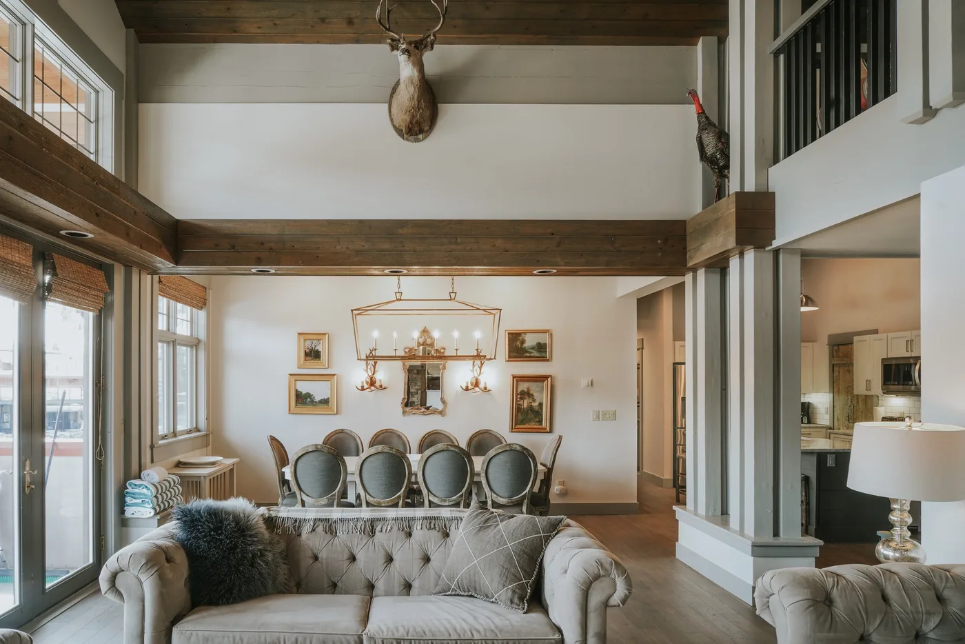 A bright living room with tufted seating and a dining area beneath a chandelier.