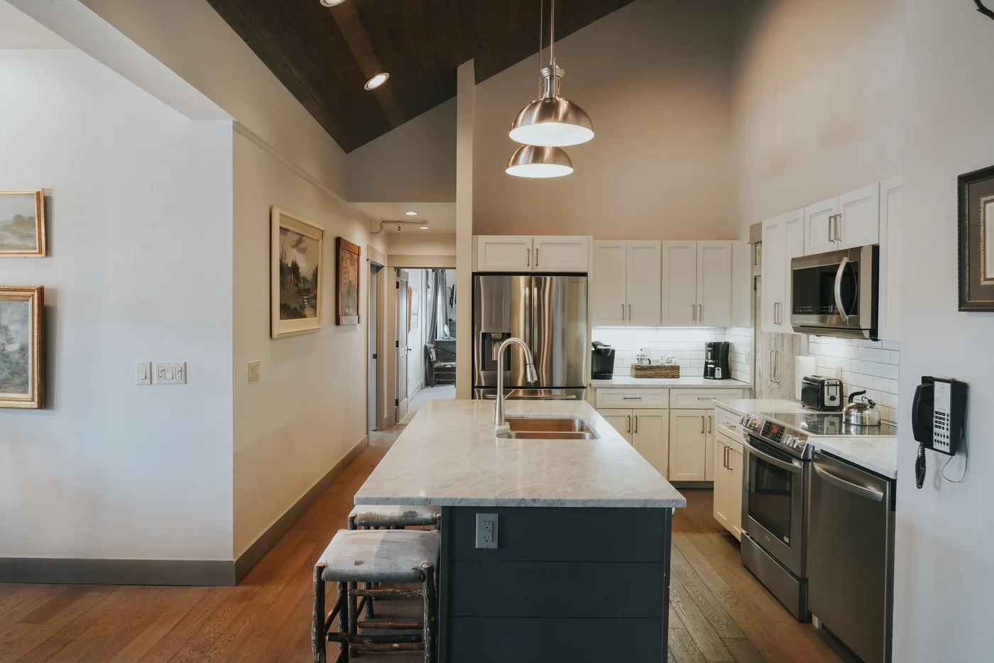 A bright kitchen with a central island, stainless steel appliances, and pendant lights.