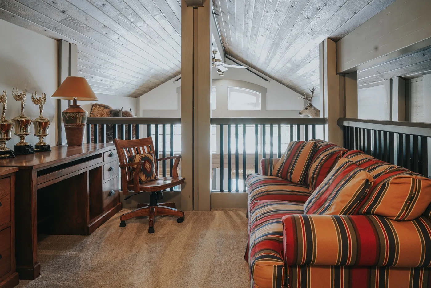 A loft-style living area with striped seating, a desk, and a railing.