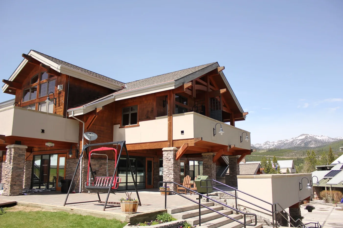 A large wood-sided house has balconies, broad windows, and a patio under a clear sky.