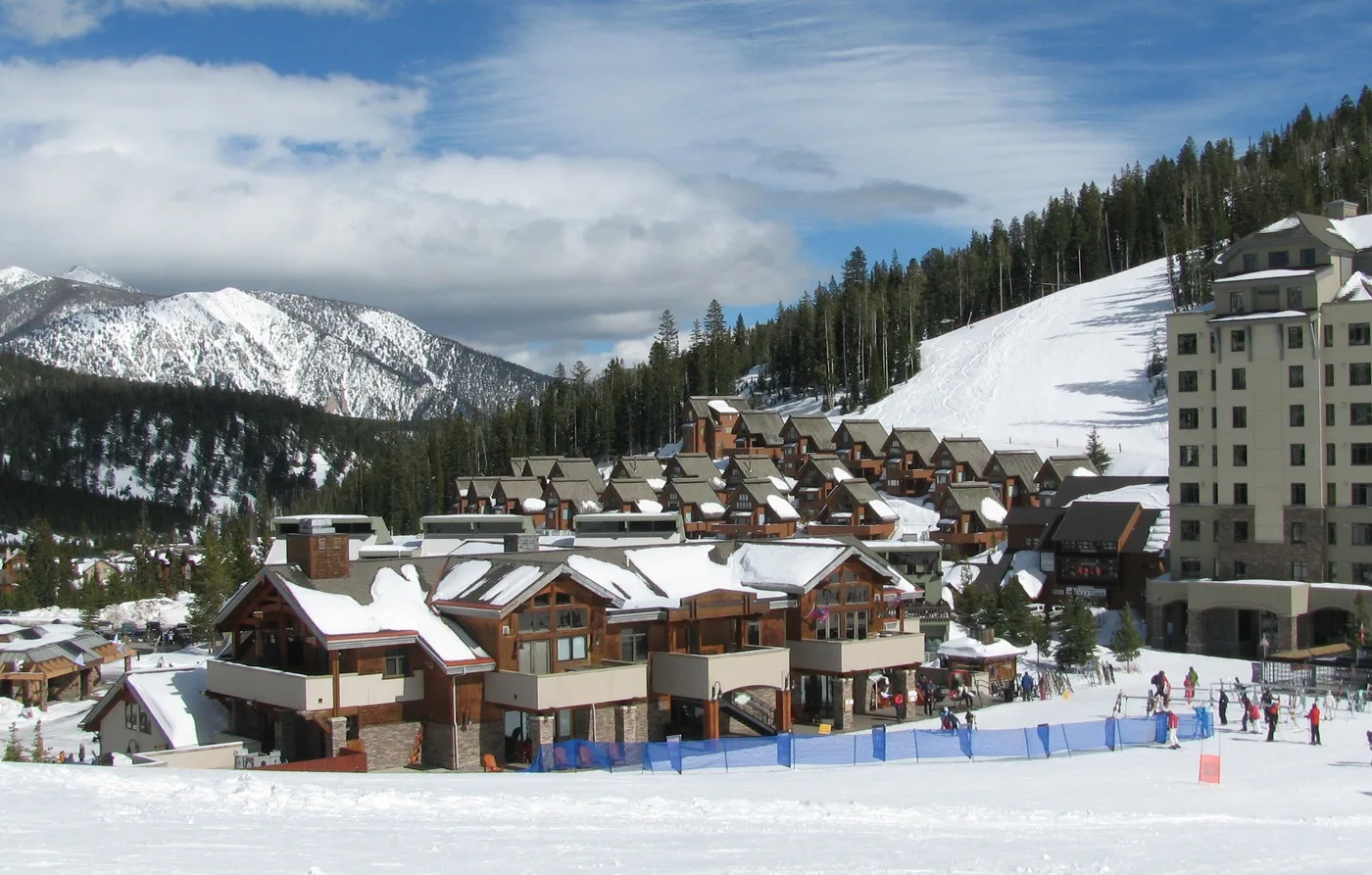 A snow-covered mountain resort with buildings beside a ski slope.