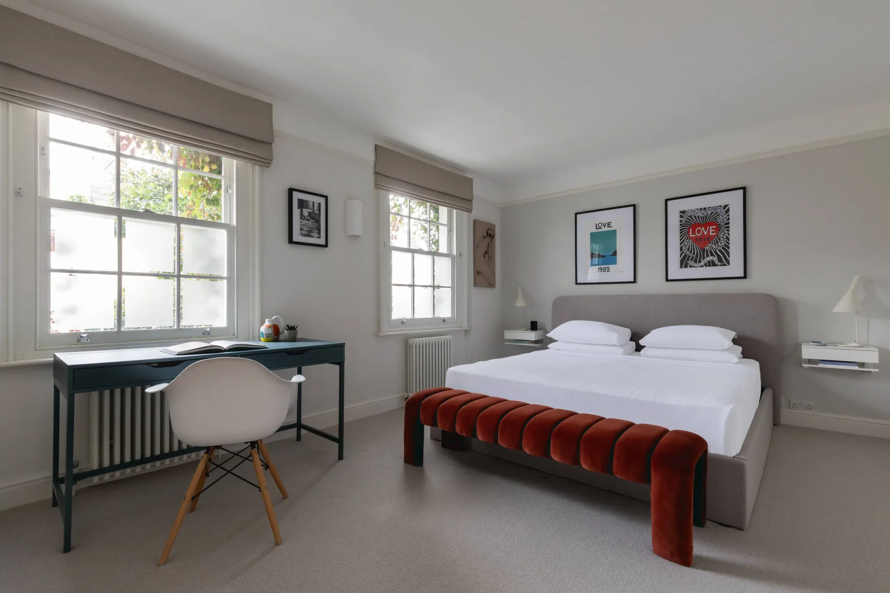 Dormitorio con una cama, un escritorio y dos ventanas luminosas.