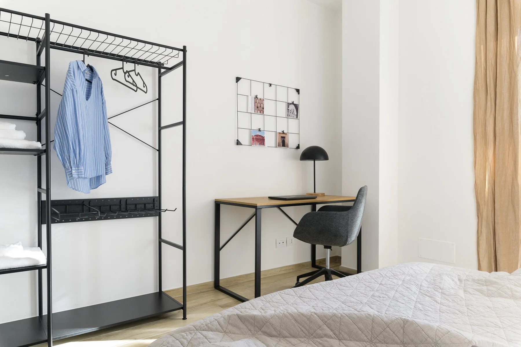 Un dormitorio luminoso con una cama, un escritorio y un perchero abierto.