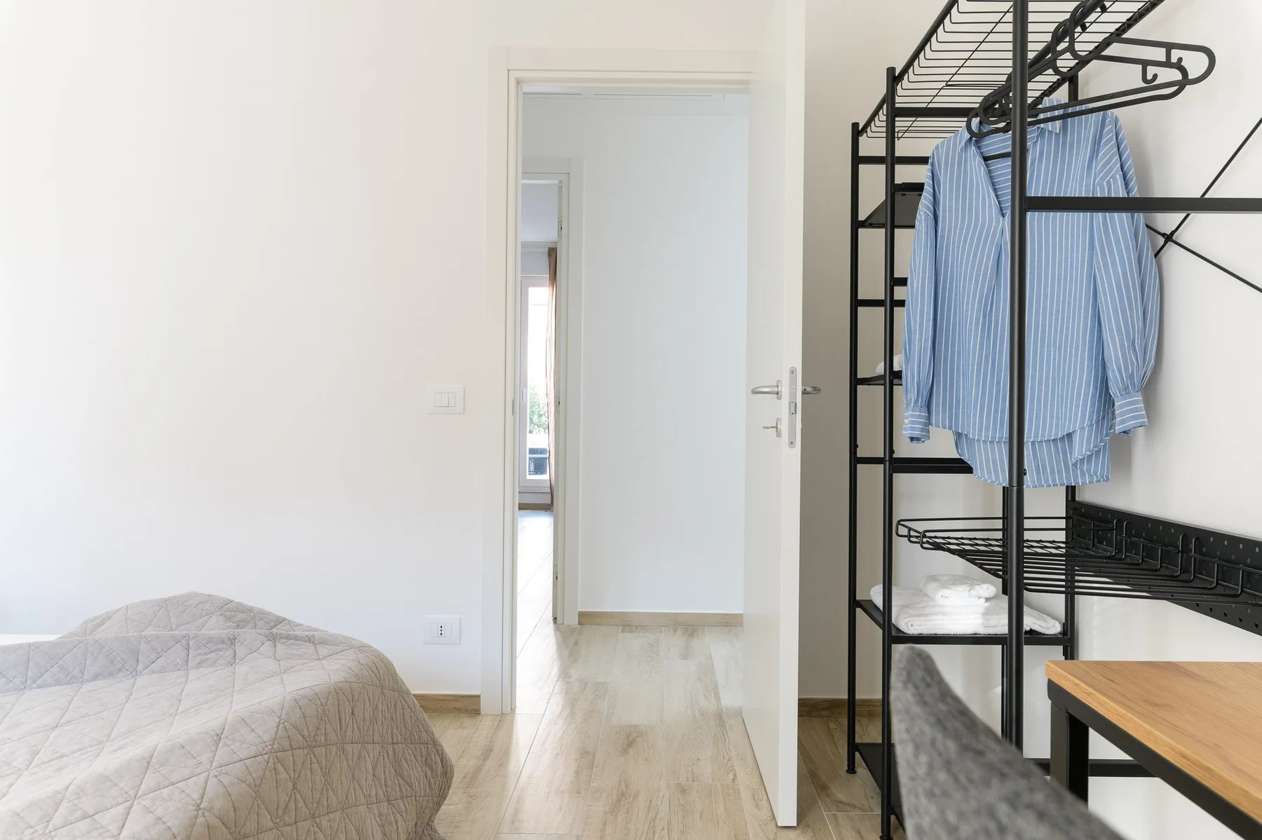 Un dormitorio con una cama y un perchero abierto junto a la puerta.