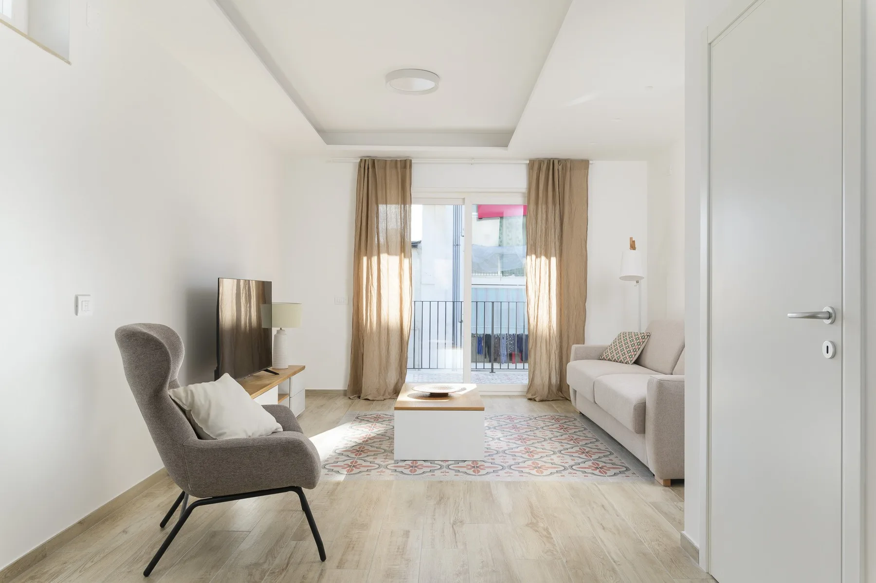 Una sala luminosa con asientos, una mesa de centro y puertas de vidrio que dan a un balcón.