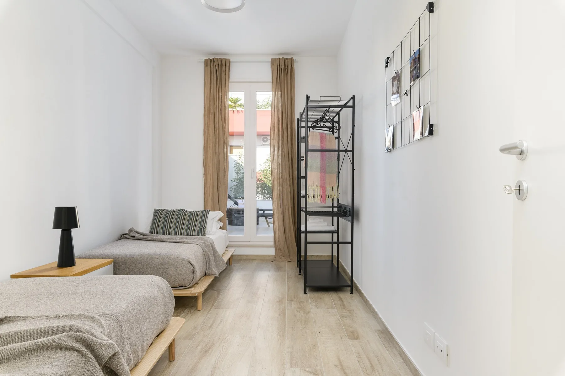 Un dormitorio luminoso tiene dos camas y una ventana alta con cortinas.