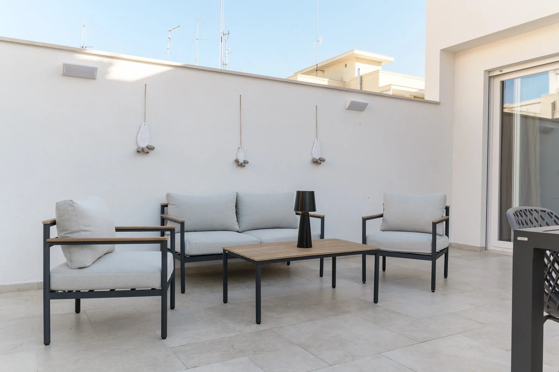Una zona de estar en una terraza con una mesa baja junto a una puerta de cristal.