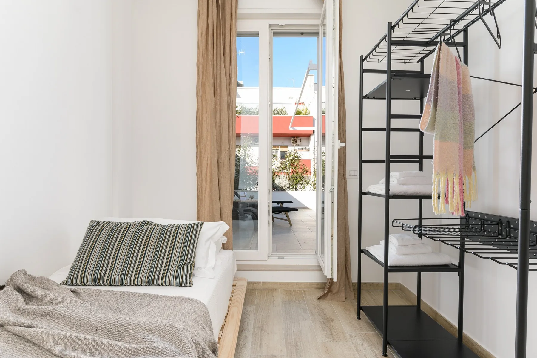 Un dormitorio luminoso con una cama junto a una estantería negra abierta y puertas de cristal.