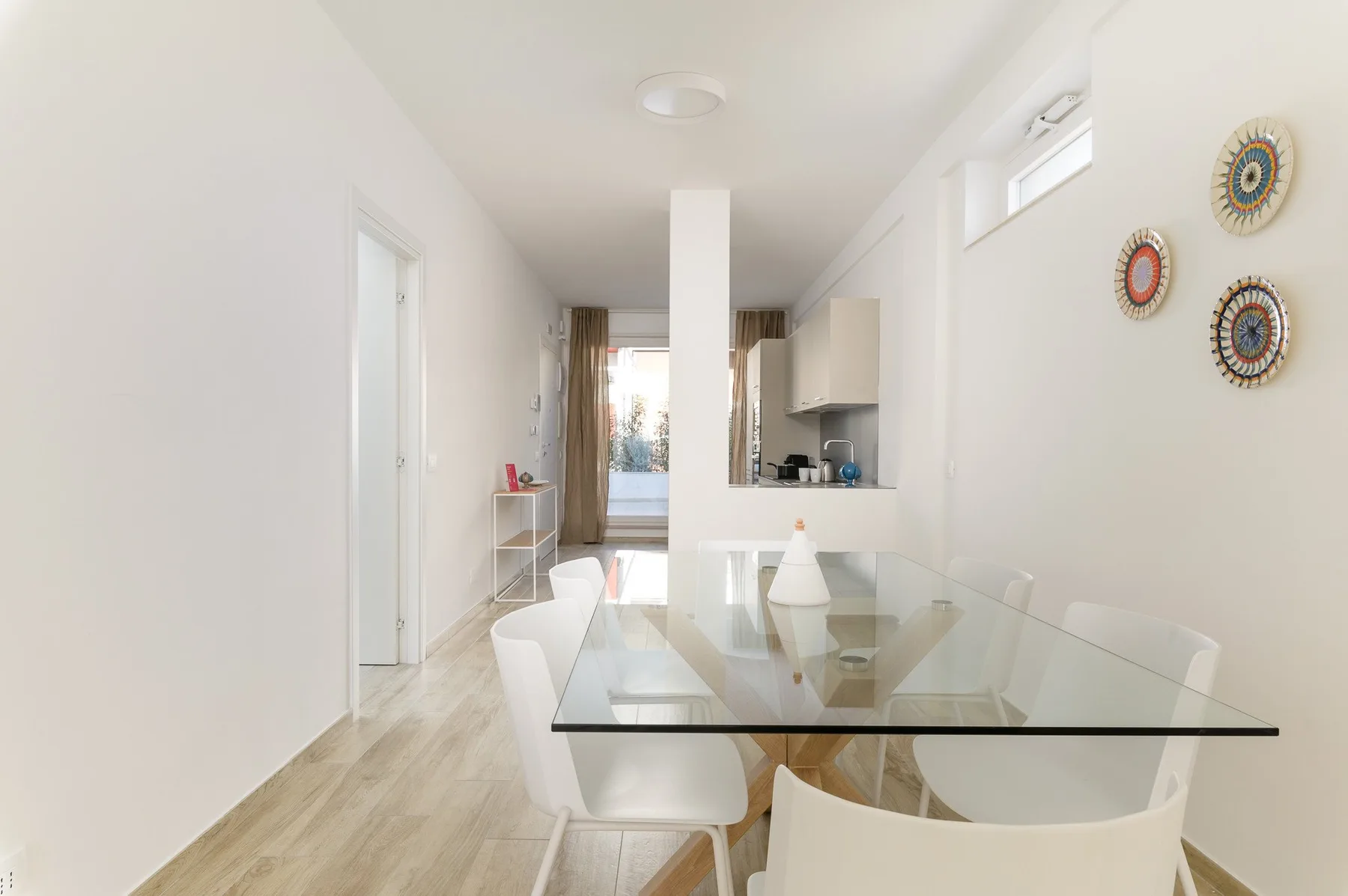 Un comedor luminoso con una mesa de vidrio y una cocina compacta al fondo.