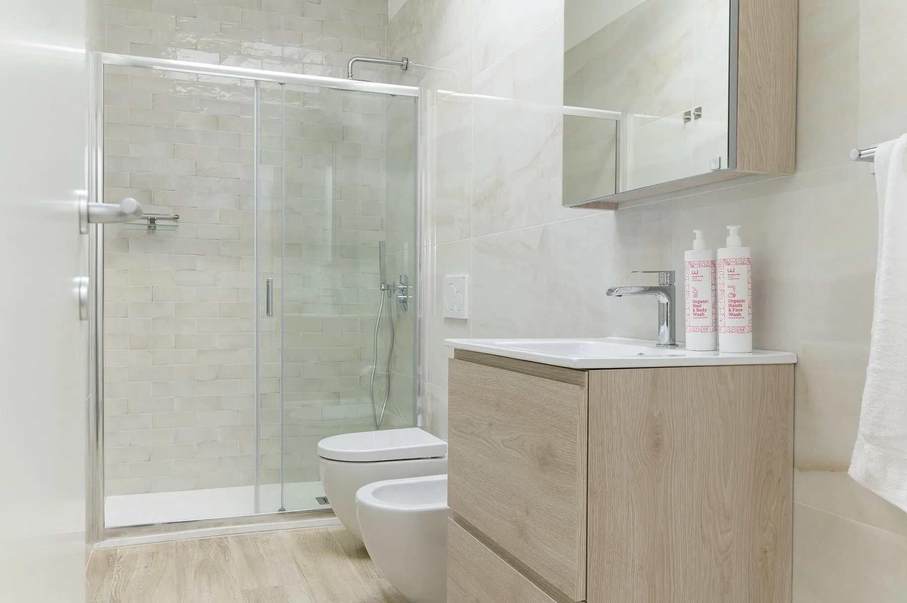 Un baño luminoso con ducha de vidrio, inodoro y lavabo con mueble.