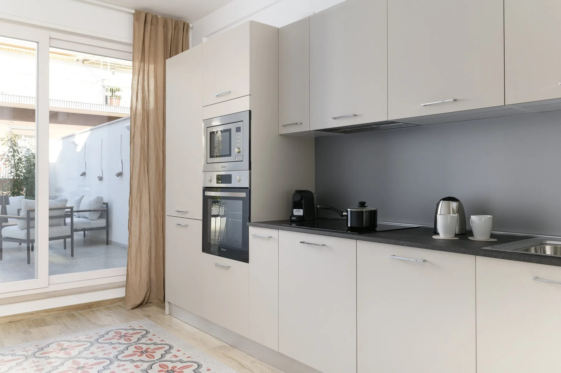 Una cocina moderna y luminosa tiene gabinetes blancos, encimeras oscuras y electrodomésticos integrados.