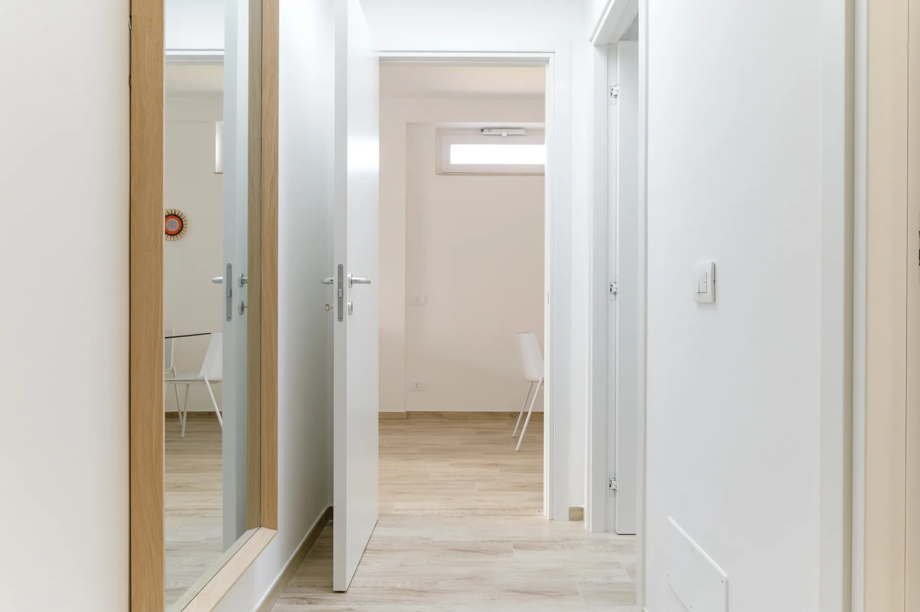 Un pasillo interior luminoso con puertas abiertas y suelo de madera clara.