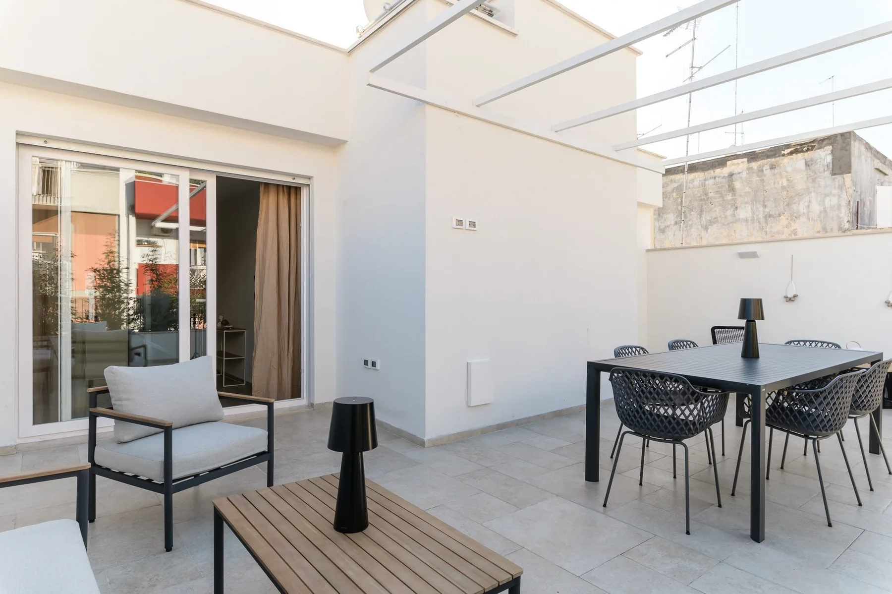 Un patio exterior luminoso con una mesa de comedor y asientos junto a puertas corredizas de vidrio.