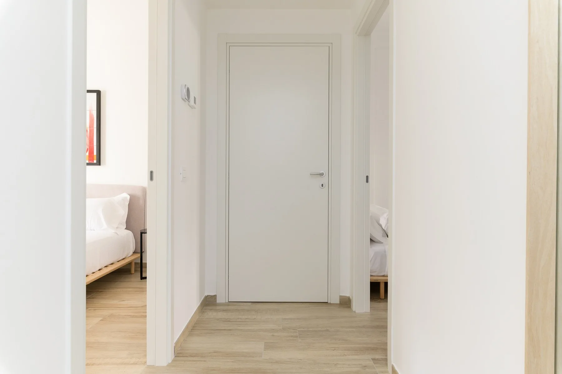 Un pasillo luminoso con una puerta cerrada y vistas a dormitorios.