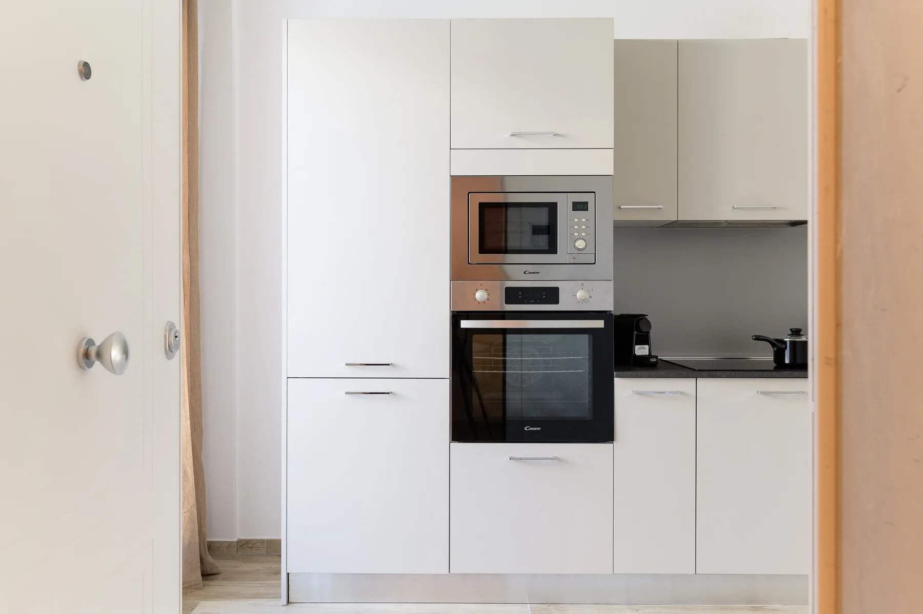 Una cocina moderna con gabinetes blancos, horno empotrado y microondas.