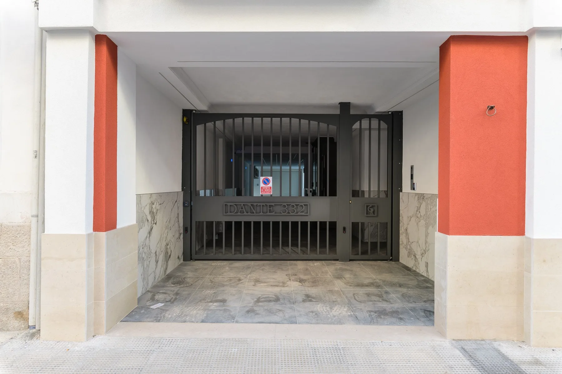 Una entrada de edificio con reja, pasillo pavimentado y paneles rojos en las paredes.