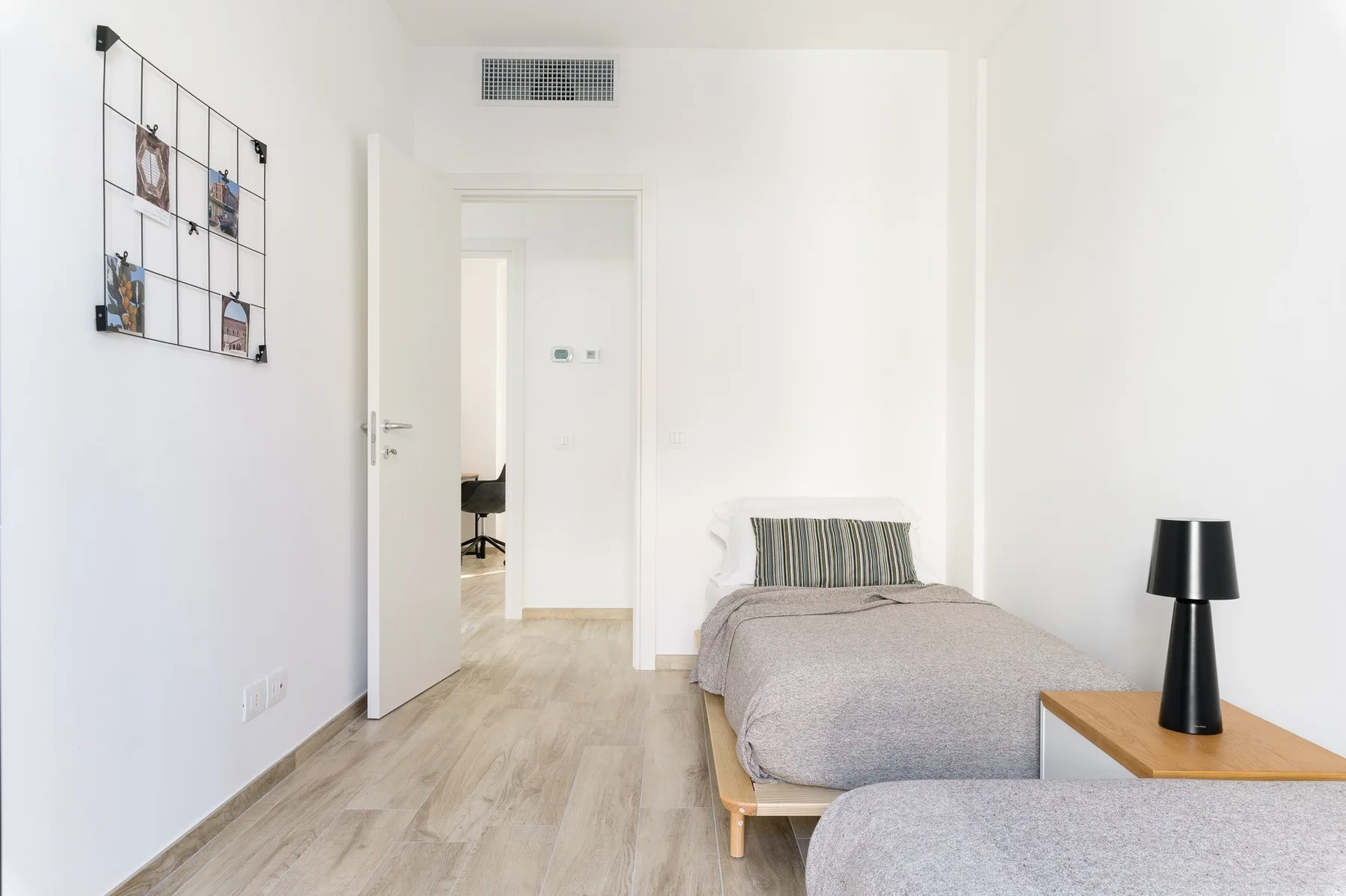 Un dormitorio luminoso con una cama individual y una lámpara negra junto a la cama.