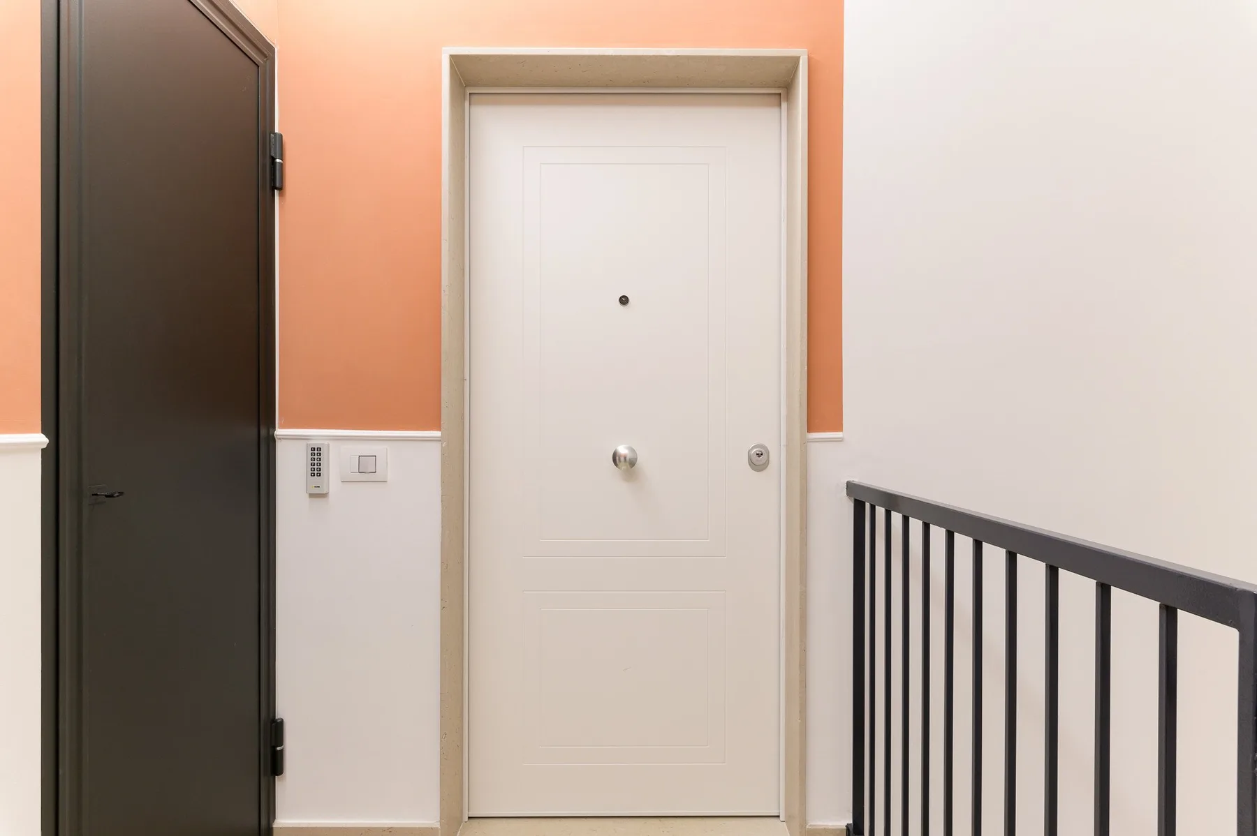 Un pasillo interior con una puerta blanca y una barandilla oscura.