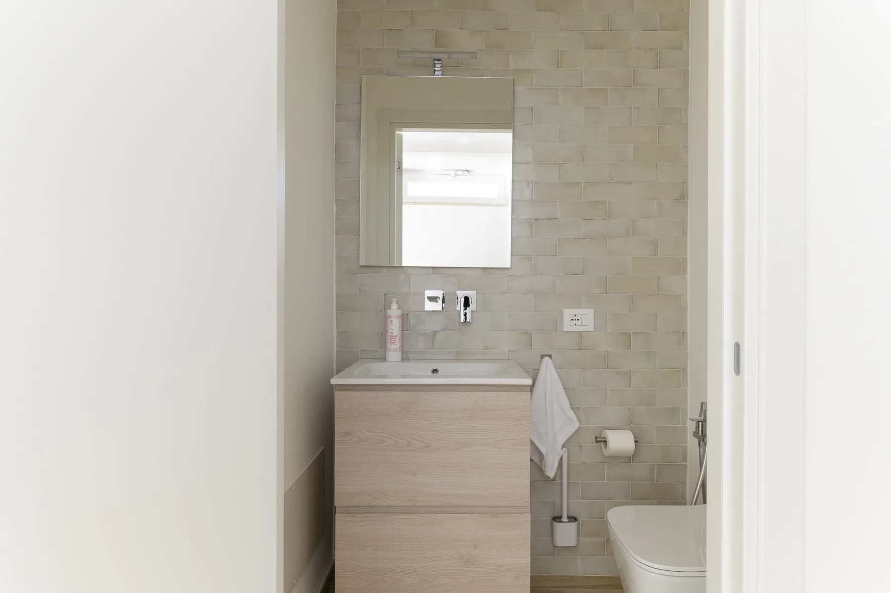 Un mueble de baño con espejo e inodoro frente a una pared de azulejos.