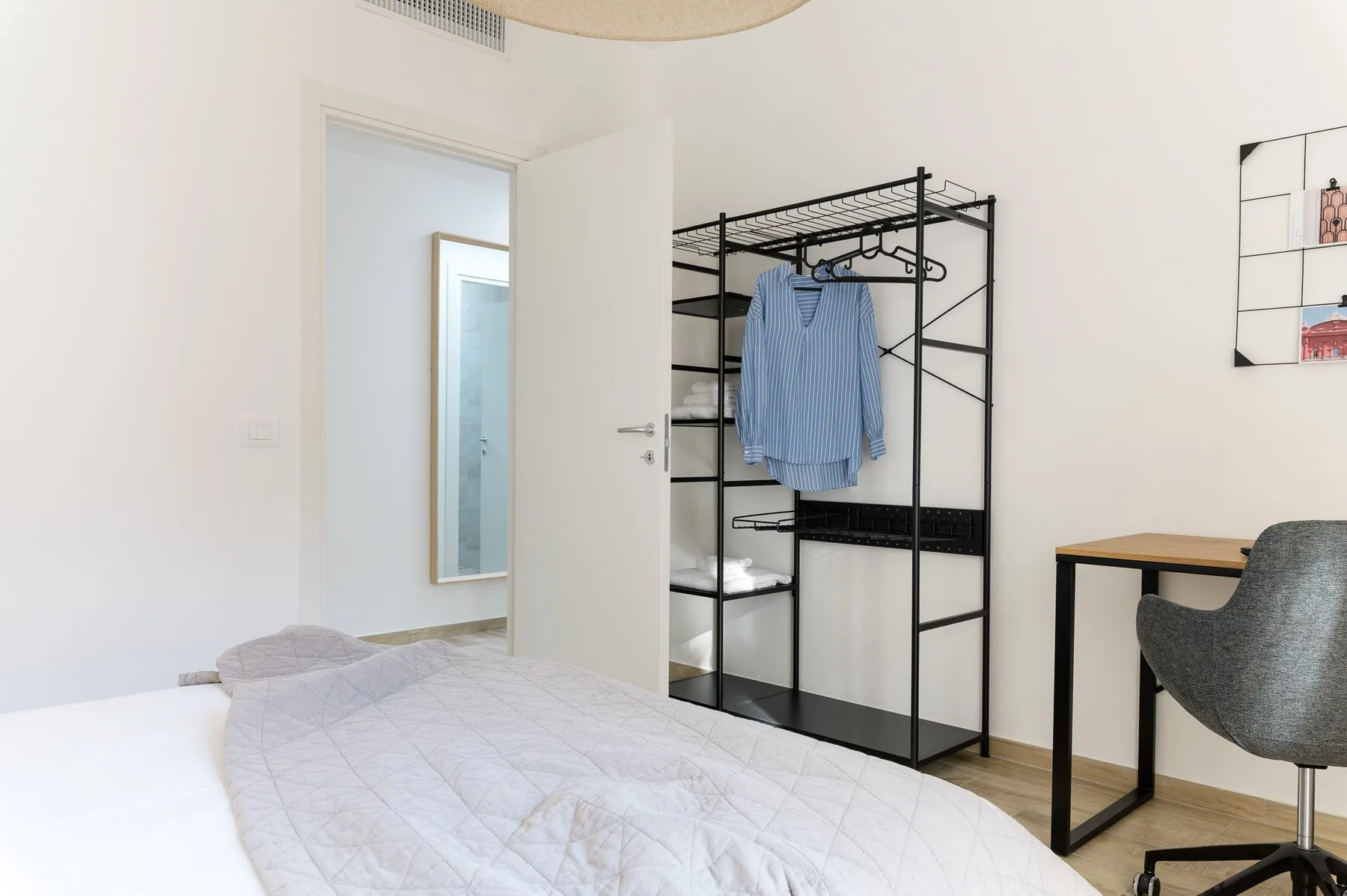 Un dormitorio luminoso con una cama y un perchero abierto junto a un escritorio.
