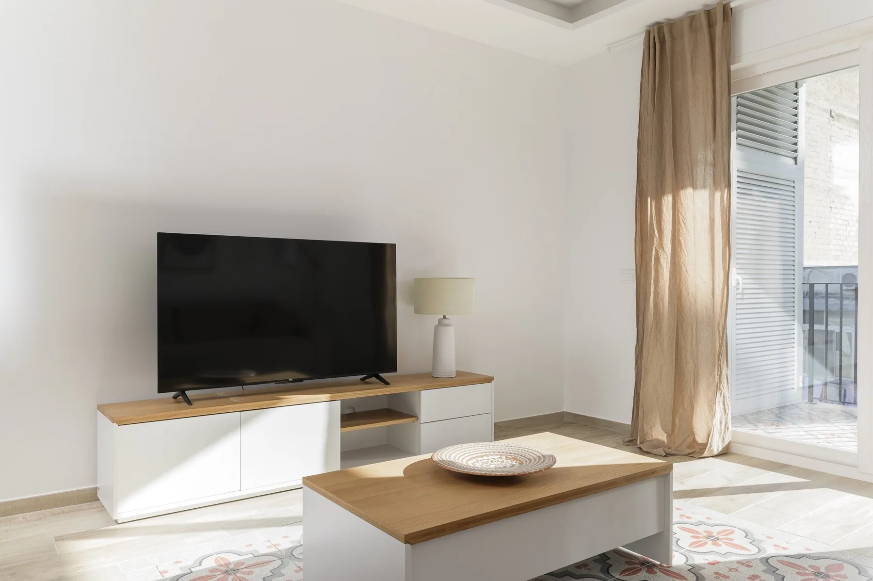 Una sala luminosa con un televisor sobre un mueble bajo y una mesa de centro.
