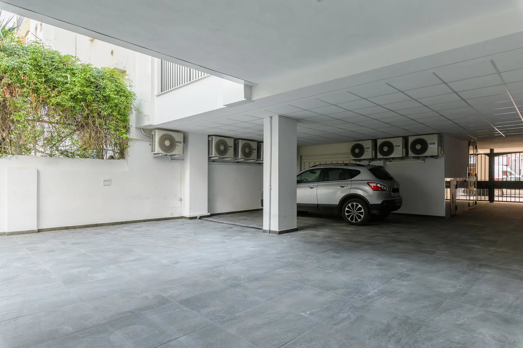Un área de estacionamiento cubierta con un automóvil estacionado y unidades de aire acondicionado en la pared.