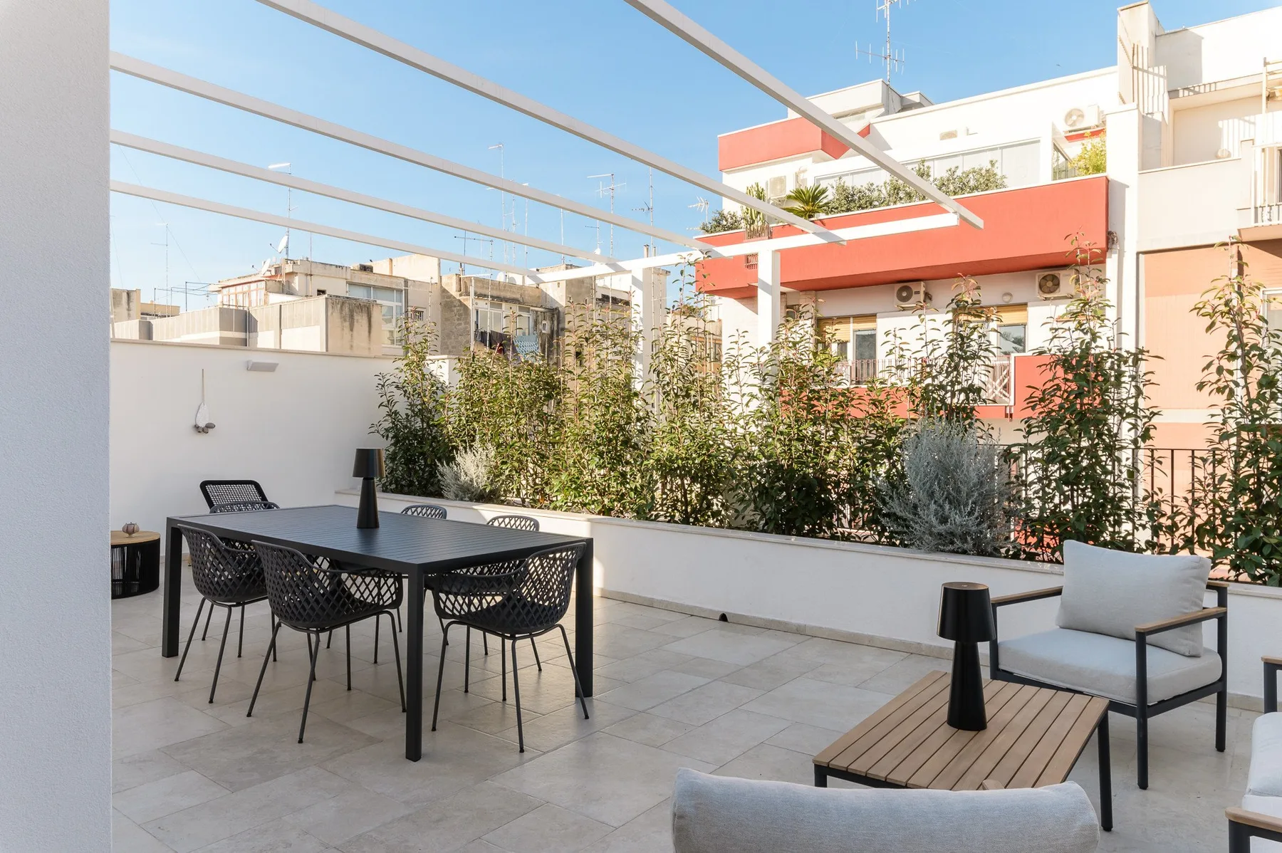 Una terraza soleada en la azotea tiene una mesa de comedor, asientos y plantas.