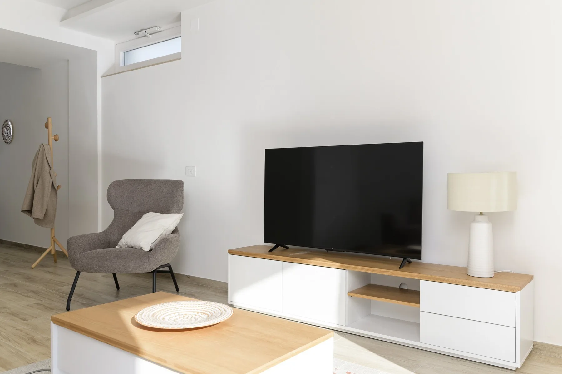 Una sala luminosa con televisión, asientos y una mesa de centro baja de madera.