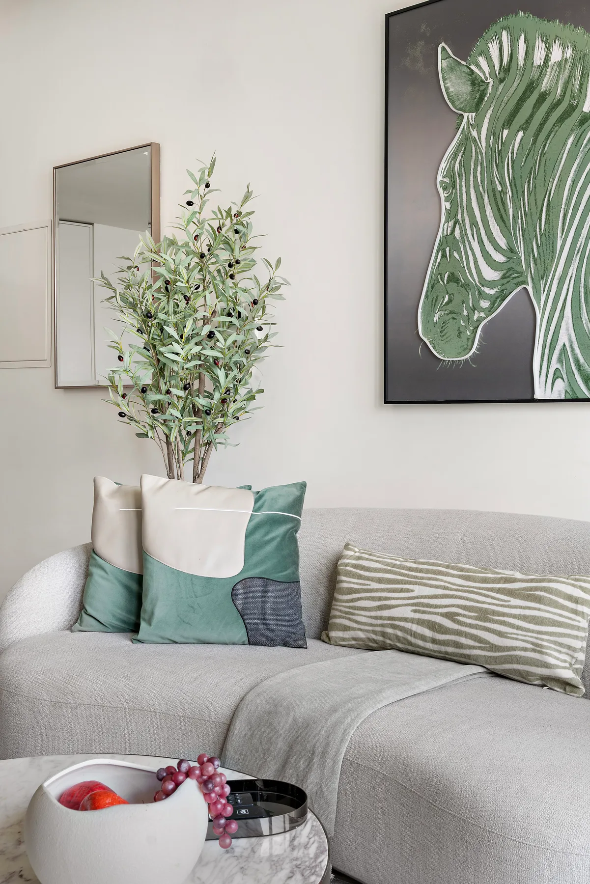 A light gray living room sofa with decorative cushions and a leafy plant.