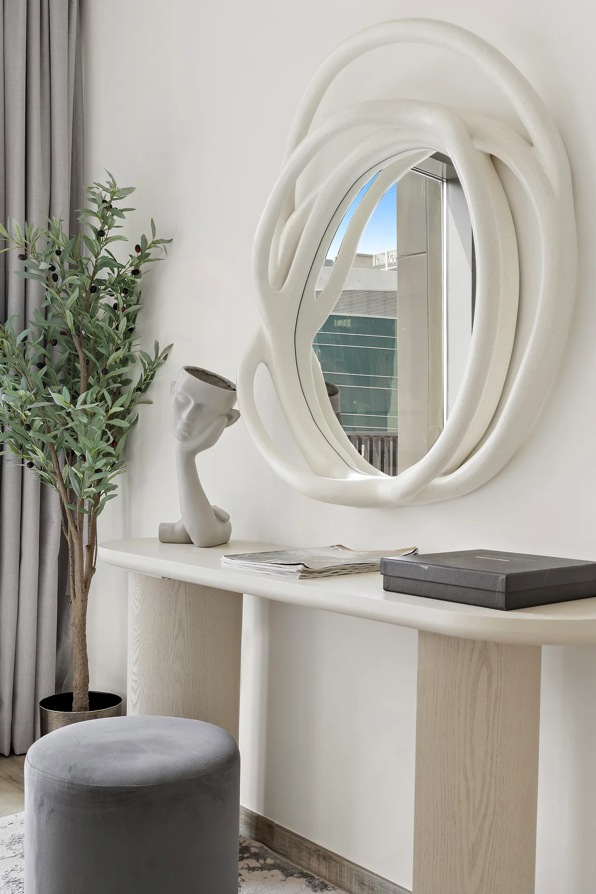 A bright interior features a sculptural wall mirror above a console table.