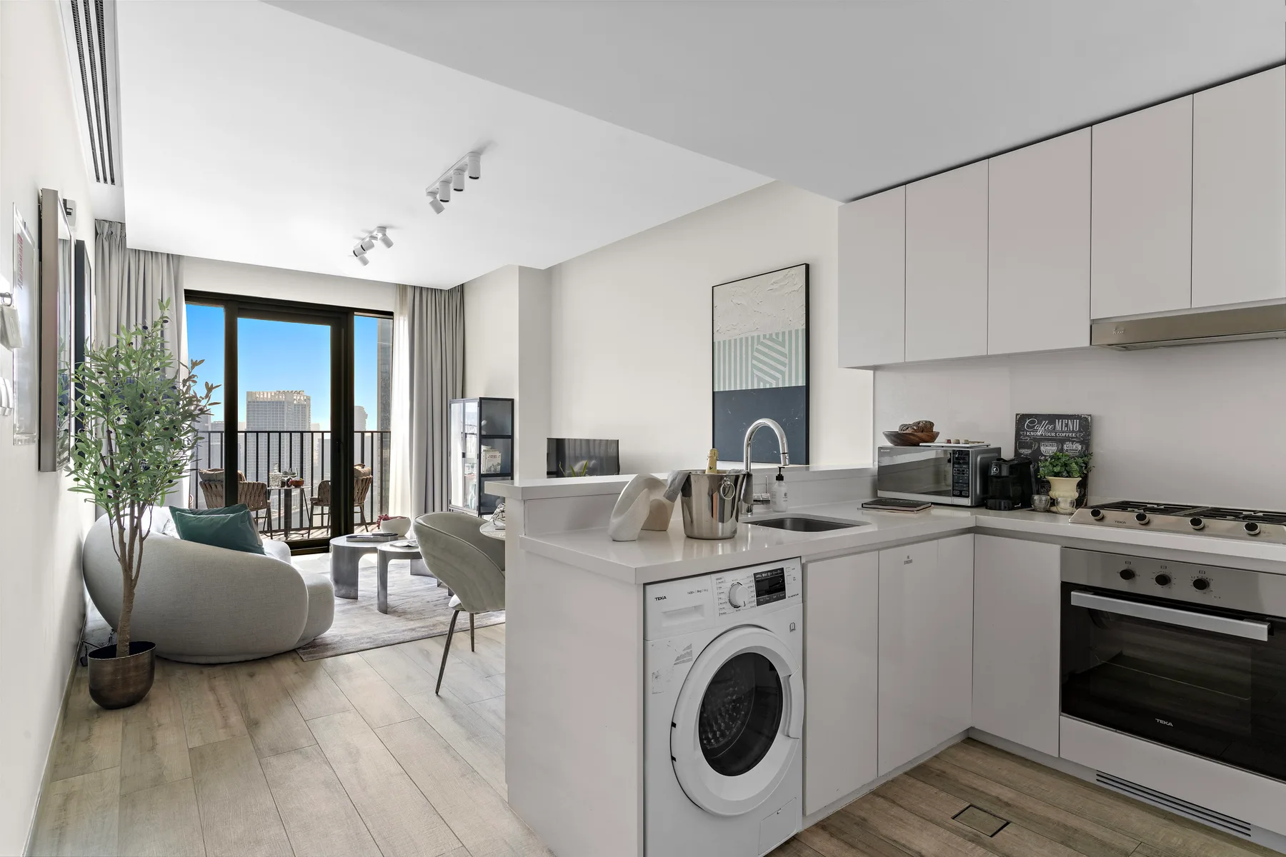 A bright open-plan kitchen and living area with a washing machine beneath the counter.