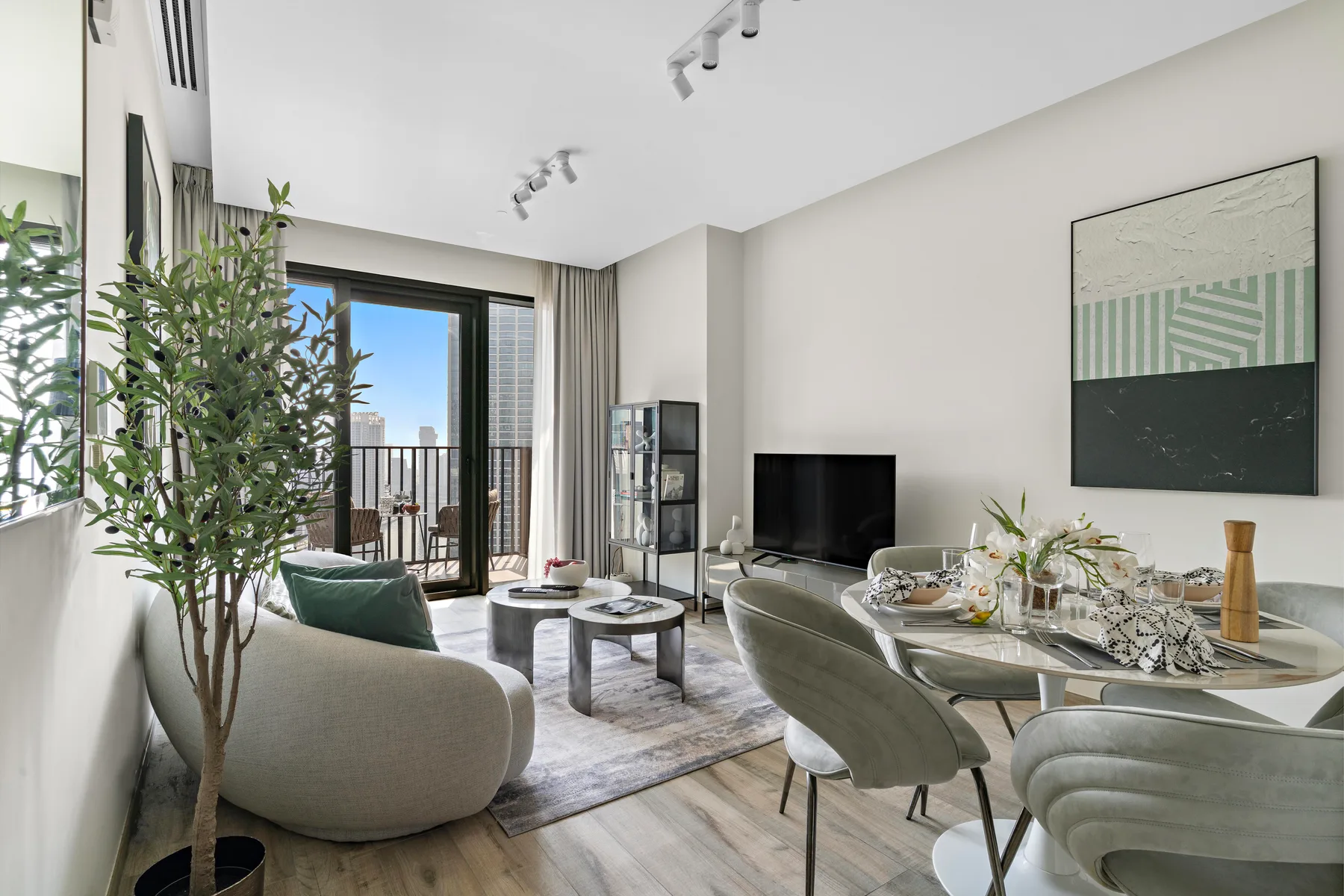 A bright living and dining room with seating, a television, and large windows.