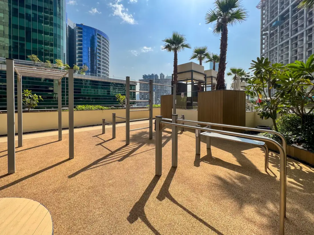 An outdoor fitness area with metal exercise bars and palm trees.