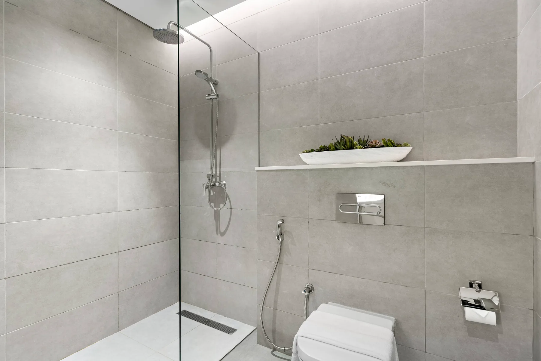 A tiled bathroom with a glass shower and wall-mounted fixtures.