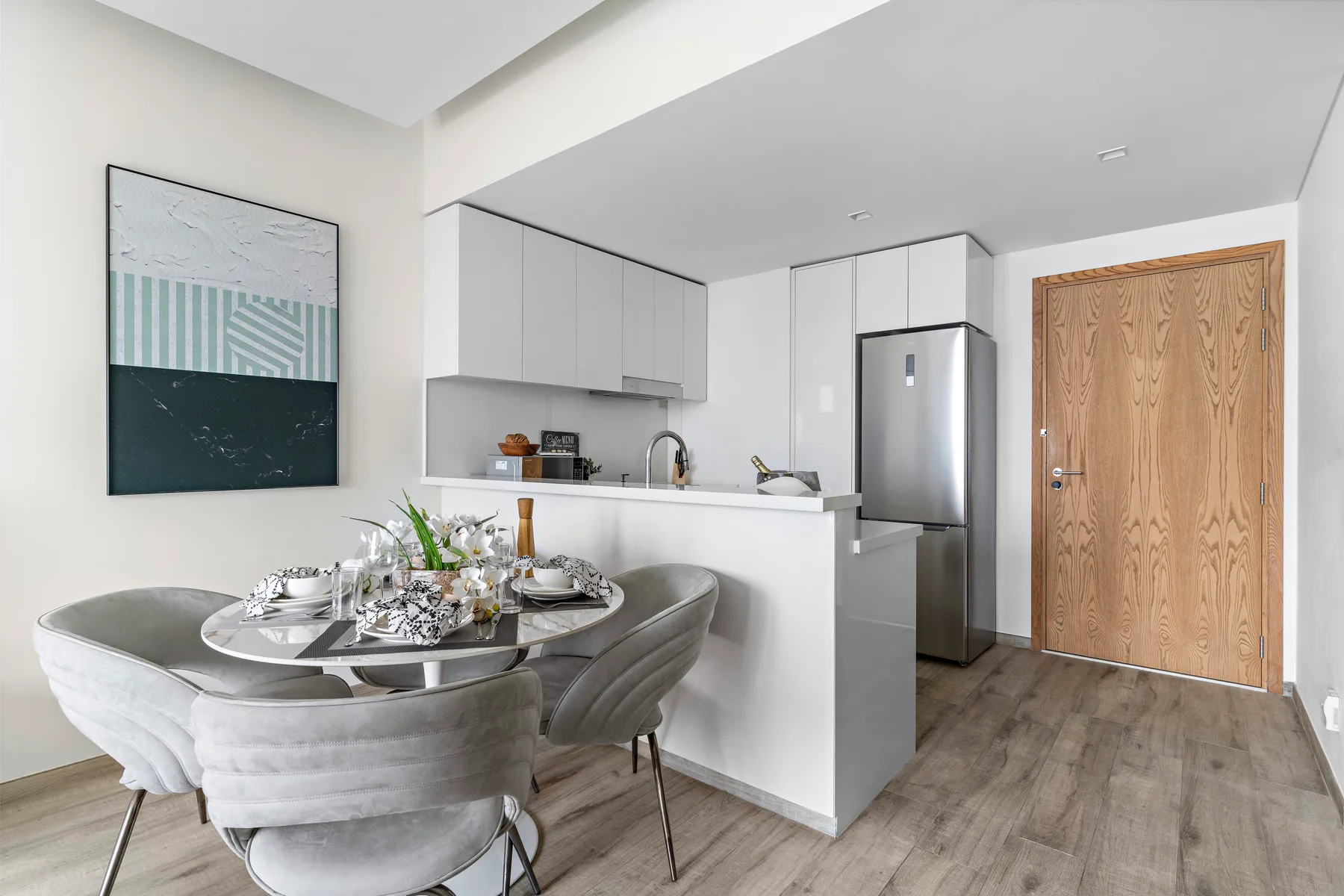 A dining area with upholstered seating and a compact white kitchen.