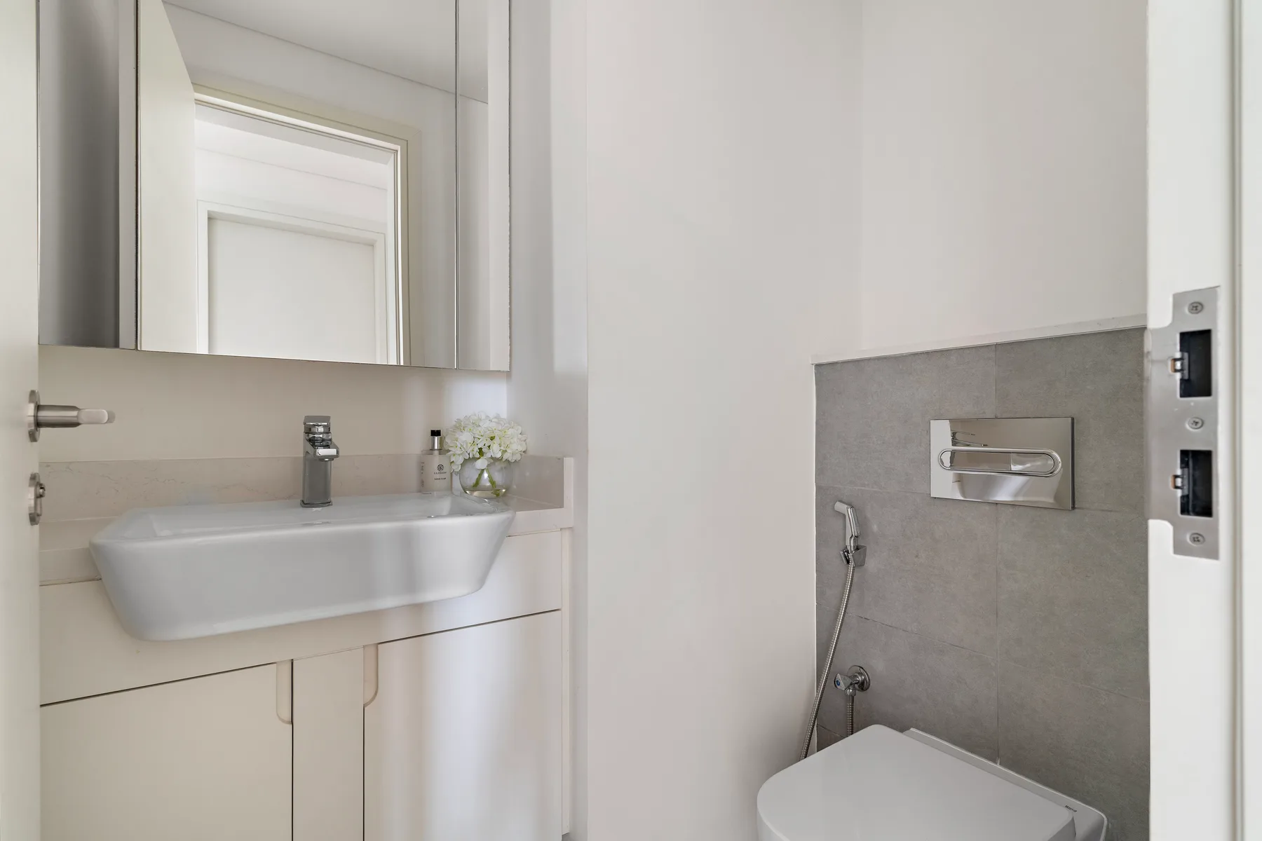 A bathroom with a sink and a wall-mounted toilet flush plate.