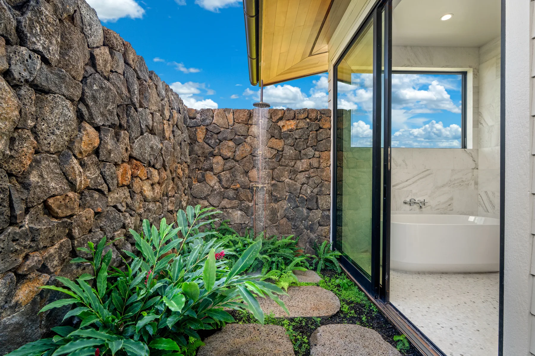A small garden patio beside a glass bathroom with a bathtub.