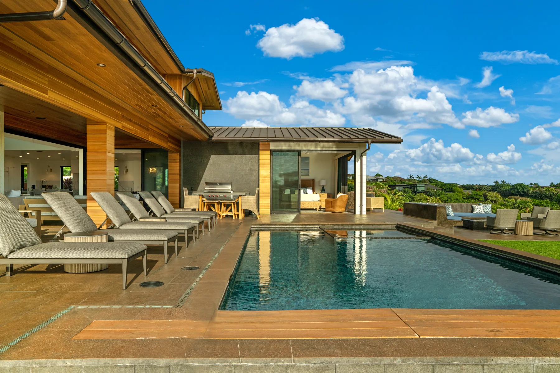 A modern house opens onto a swimming pool and an outdoor seating area.