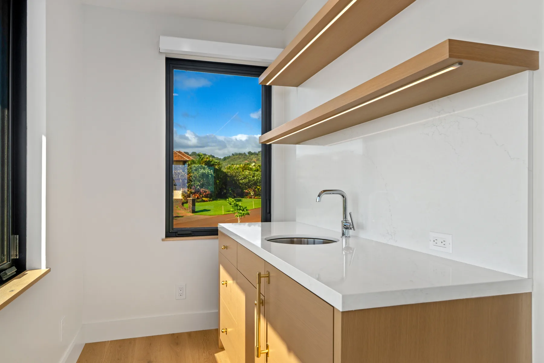 A bright kitchen with a countertop, sink, and window overlooking greenery.