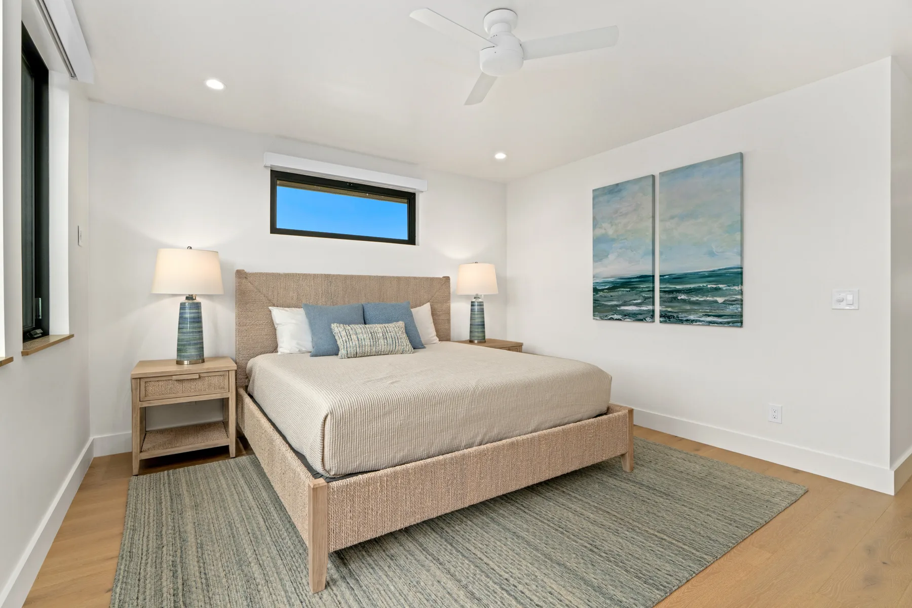 A bright bedroom with a neatly made bed and ocean-themed wall art.