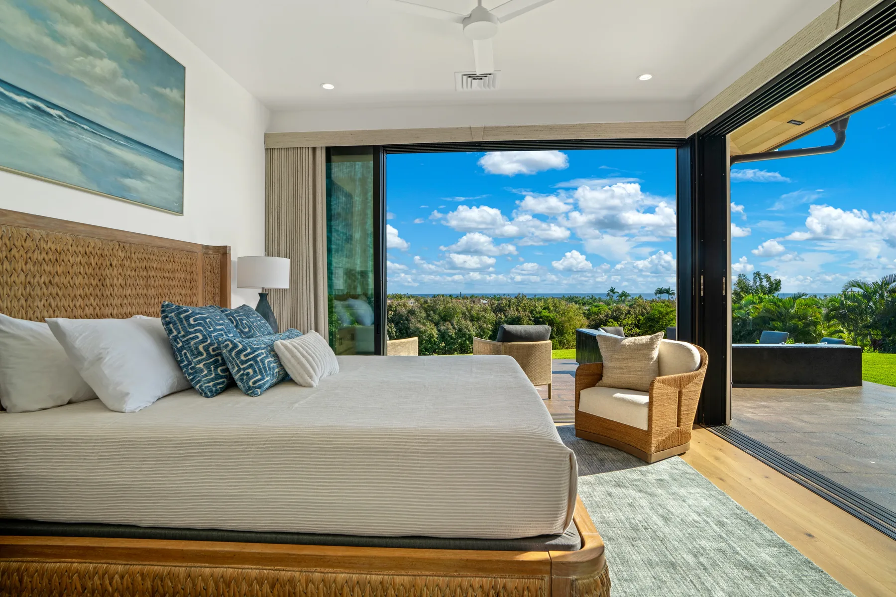A bright bedroom opens onto a patio with seating and a wide landscape view.