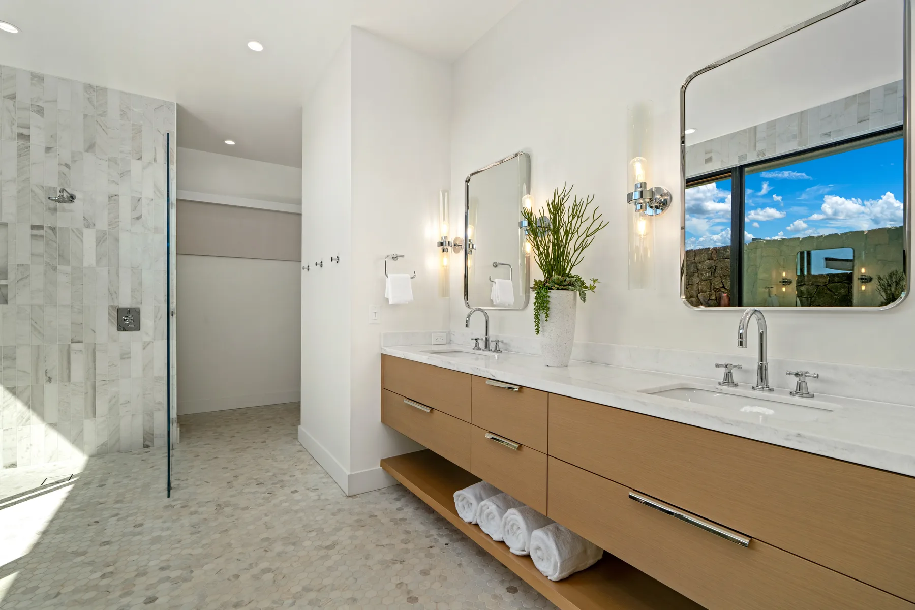 A bright bathroom features a long vanity with two sinks and a glass shower.