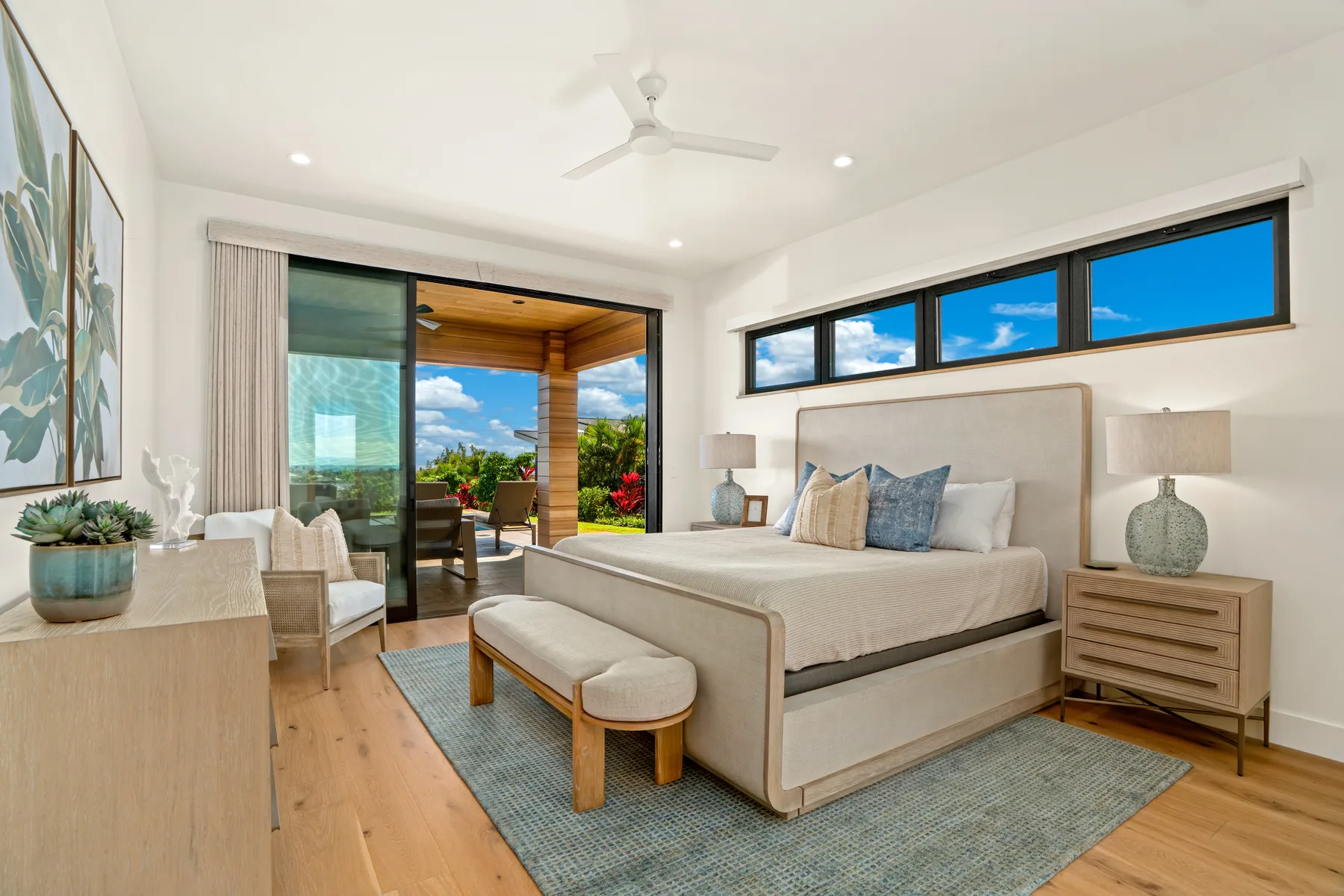 A bright bedroom with a bed, bedside tables, and windows overlooking a patio.