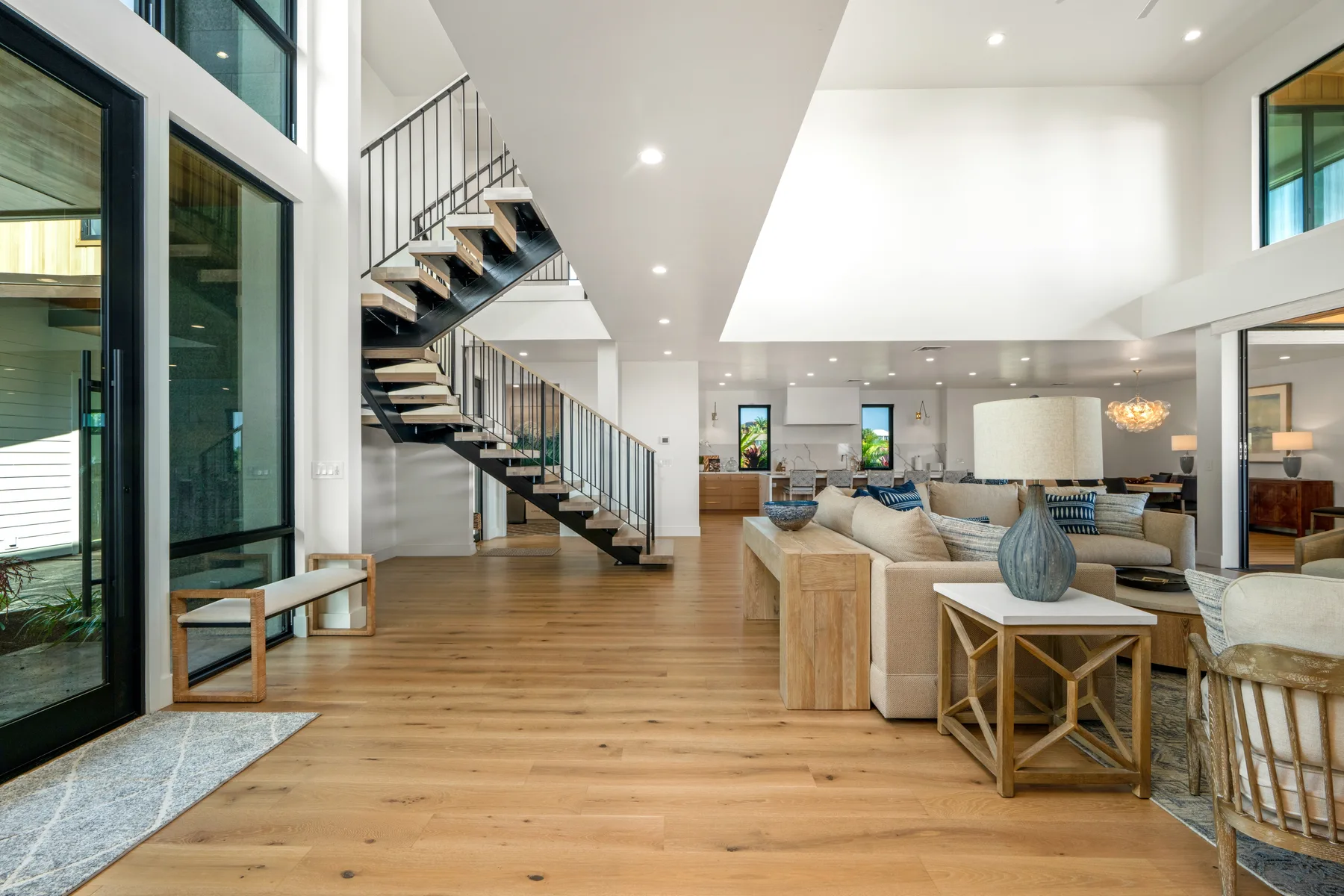 A bright open-plan living room with wood floors and a staircase.